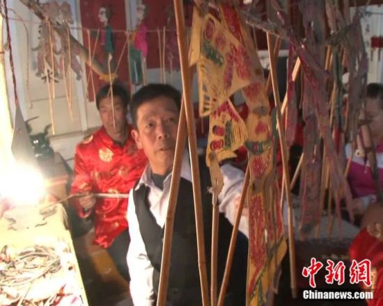 刘国天(左二)在表演现场挂皮影。(资料图)通渭县宣传部供图