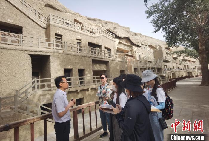 为期六周的“香港青年敦煌实习计划2023”日前在甘肃敦煌举办。图为参加实习的学生在听专家讲解莫高窟知识。　中新社记者 索有为 摄